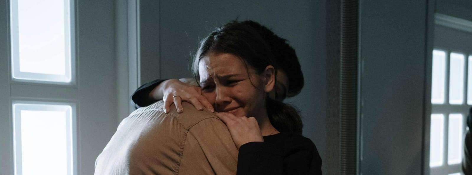 Ženska v solzah se v objemu nasloni na ramo bližnje osebe